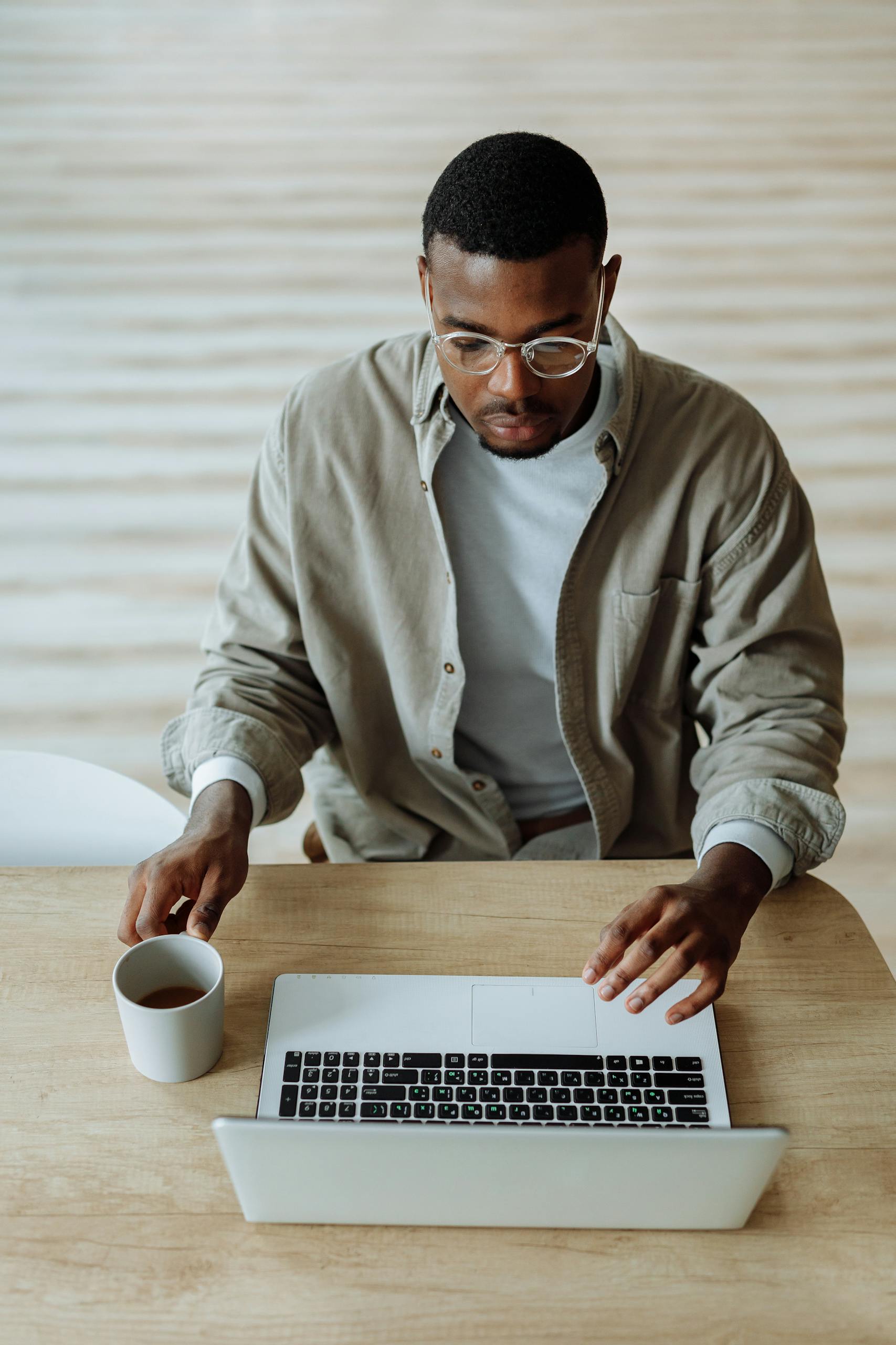 High angle view of a man working on a laptop with a coffee cup indoors, showcasing remote work lifestyle.